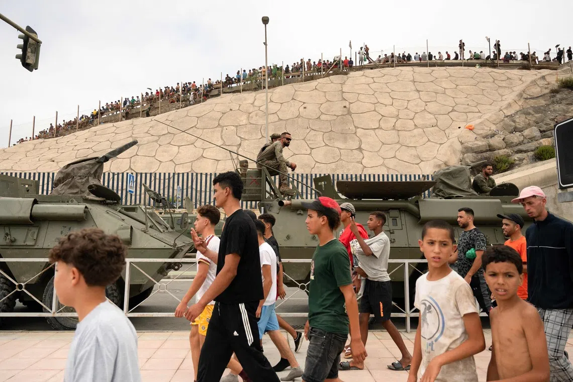 Migrants walk past Spanish military personal in the border between Morocco and the Spain’s north Africa’s Ceuta enclave on July 31.