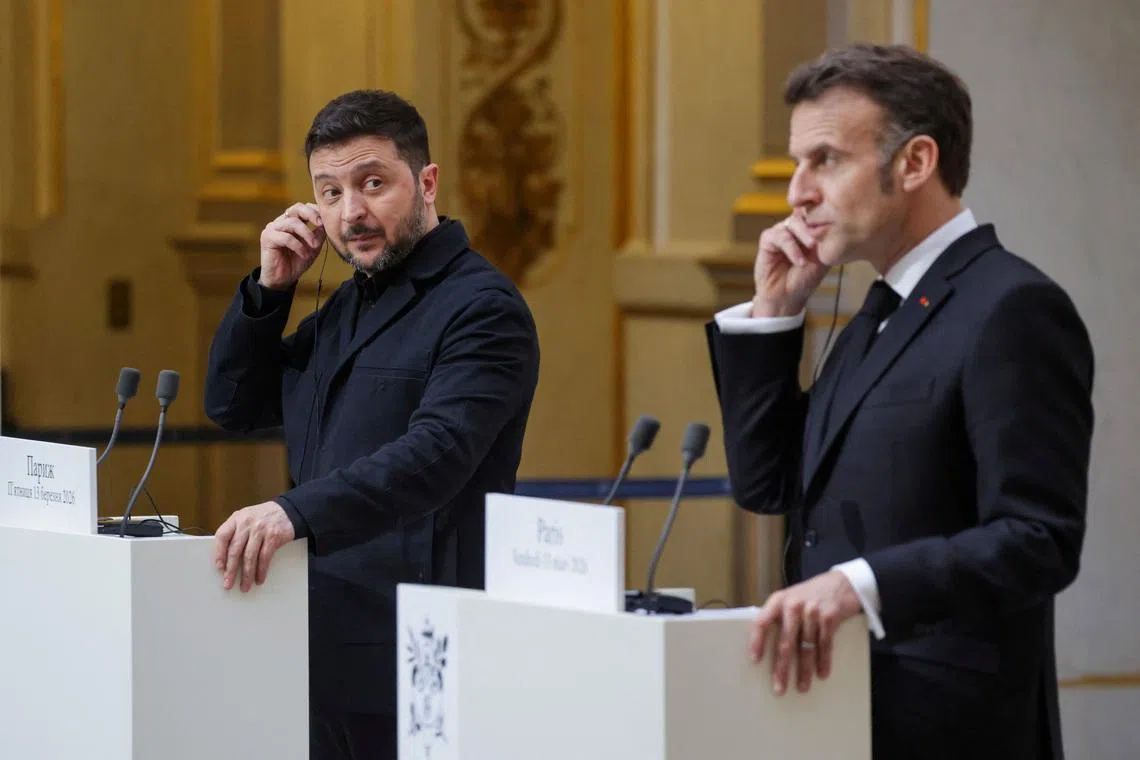Ukraine's President Volodymyr Zelensky (L) and France's President Emmanuel Macron (R) put on a earpiece as they deliver a speech during a joint press conference, in Paris, March 13, 2026.  LUDOVIC MARIN/Pool via REUTERS