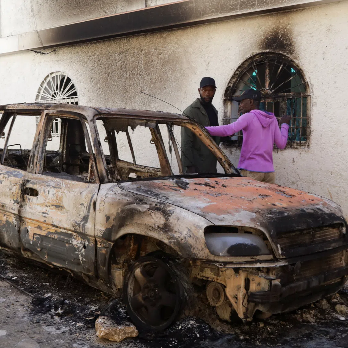 People stand next to a burned car after a fatal overnight raid by an armed gang, on the outskirts of Port-au-Prince, in Kenscoff, Haiti, August 24, 2026. REUTERS/Fildor Pq Egeder