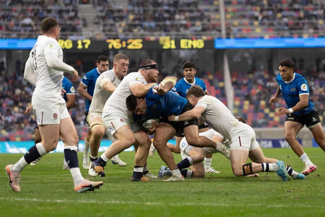 Argentina's flanker Joaquin Oviedo (C) is tackled by England's prop Joe Heyes (L) during the Rugby Union Nations Championship match between Argentina and England at Unico Madre de Ciudades stadium in Santiago del Estero, Argentina, on July 18, 2026. Argentina players wear a blue jersey as a tribute to the Argentina national football team that defeated England with goals by Diego Maradona at the Mexico 1986 World Cup. (Photo by Juan Gasparini / AFP)