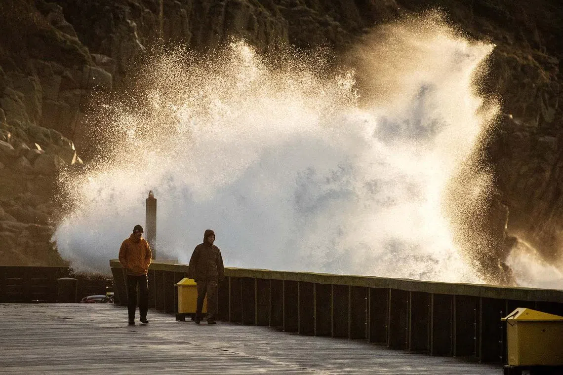 People walking as waves crash on the shore in the aftermath of Storm Pia on Dec 22, 2023, which hit Denmark the day before on Thursday, in Hammerhavn, on the island of Bornholm, Denmark.