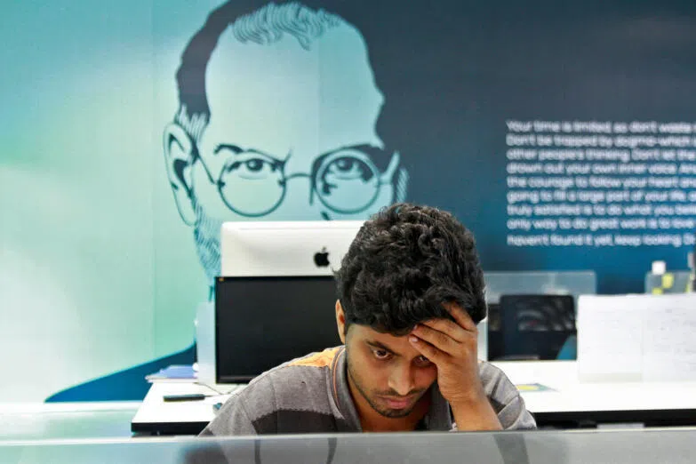 An employee works on a computer terminal against the backdrop of a picture of late Apple co-founder Steve Jobs in the southern Indian city of Kochi on Oct 13, 2012.
