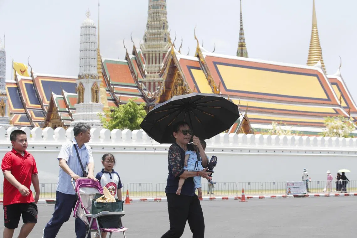 A woman uses an umbrella and electric fan to protect an infant from the sunlight during hot weather outside the Temple of the Emerald Buddha in Bangkok on 29 April 2024.