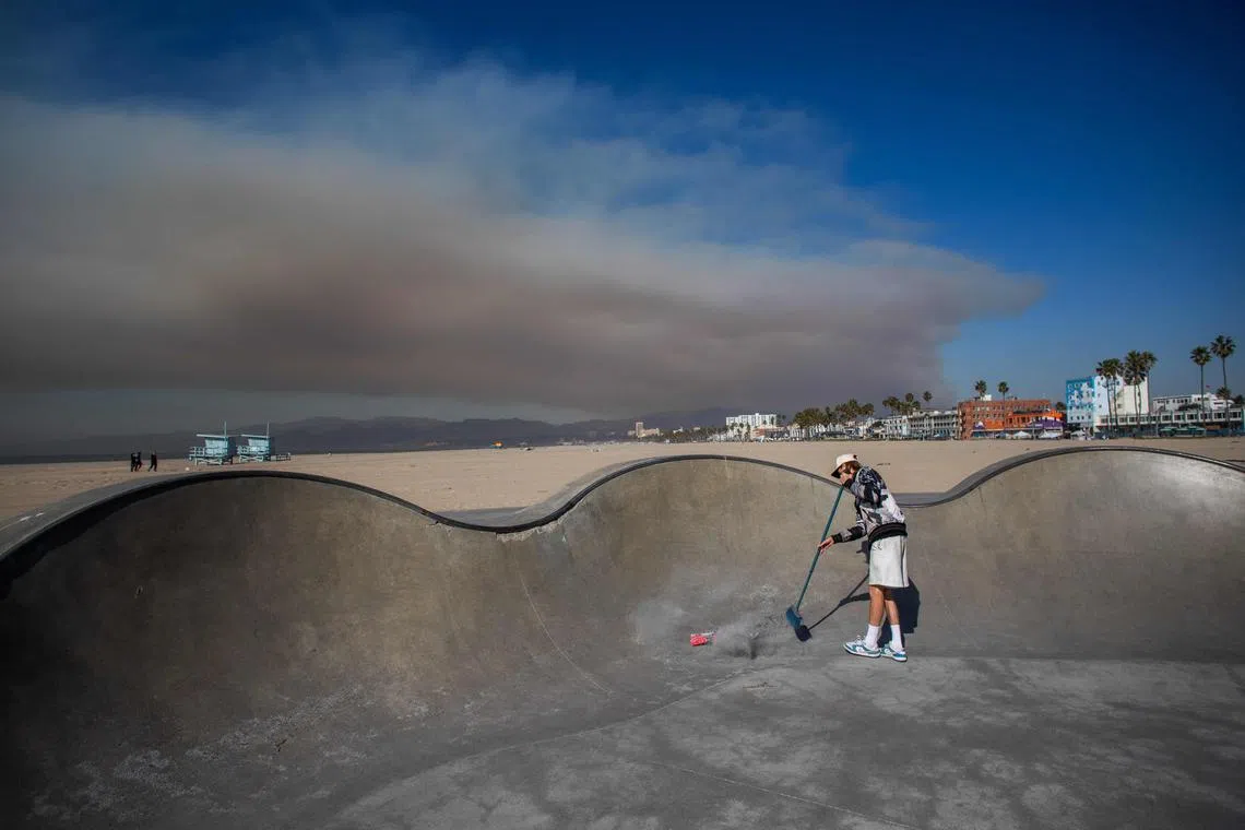 Skateboarder Haden Mckenna sweeping ash from the Venice Skatepark as smoke rises from the Palisades Fire wildfires in the background on Jan 11 in Los Angeles. 