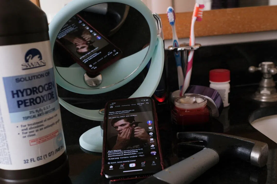 This illustration photo shows a video of male TikTok influencer hammering his cheekbone, playing on a smartphone in a bathroom next to a bottle of hydrogen peroxide and a hammer in Los Angeles, April 11, 2025. Hankering for a perfectly angular jaw, a male TikTok influencer hits his cheekbones with a hammer -- part of the popular online “looksmaxxing” trend that promotes unproven and often dangerous techniques to boost sexual appeal. Looksmaxxing influencers -- part of an online ecosystem dubbed the "manosphere" -- have surged in popularity across social media, capitalizing on the insecurities of young men eager to boost their physical attractiveness to women. (Photo by Chris DELMAS / AFP)