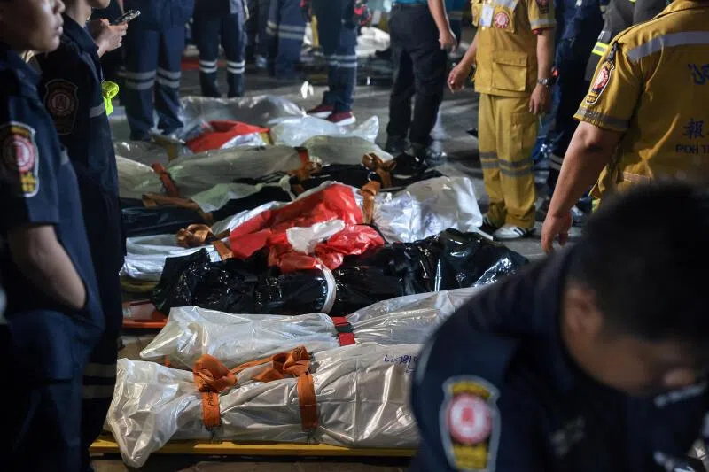 Members of emergency personnel working next to covered bodies at the site of a deadly fire at a pub in Bangkok, Thailand.