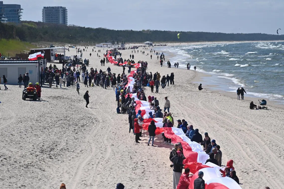 People gathering around the longest flag in Poland, at a beach during the National Flag Day in Miedzyzdroje, Poland on May 2, 2023. The 2.5 kilometers flag was brought to the beach in two parts. 