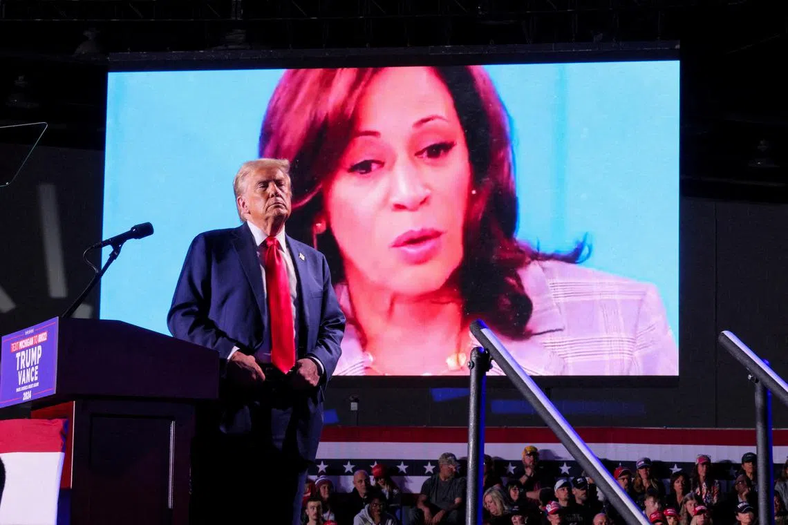 FILE PHOTO: Republican presidential nominee and former U.S. President Donald Trump looks on as Democratic presidential nominee and U.S. Vice President Kamala Harris' face appears as a video plays on a screen, during a rally at Huntington Place in Detroit, Michigan, U.S. October 18, 2024.  REUTERS/Brian Snyder/File Photo