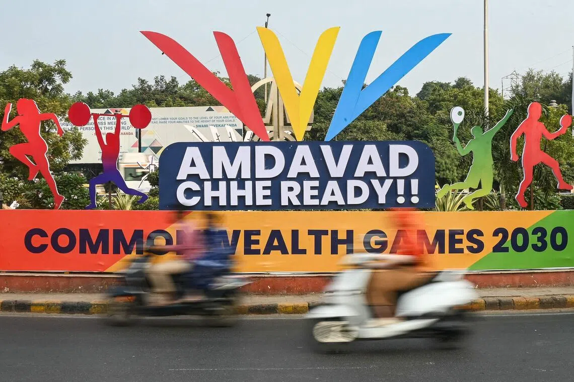 Commuters ride past a signboard cut-out advertising the 2030 Commonwealth Games in Ahmedabad on Nov 29, 2025. 