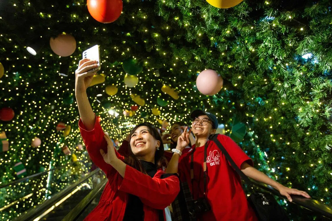 Compradores posam para uma selfie com seus celulares enquanto sobem em uma escada rolante passando pelas decorações de Natal em Bangkok em 23 de dezembro de 2024. (Foto de Candida NG / AFP)