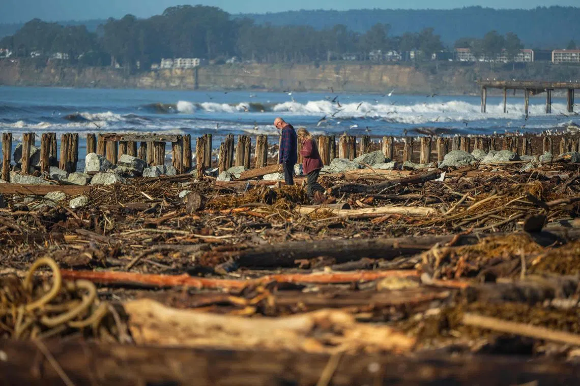 People walk among drift wood and storm debris on Rio Del Mar Beach in  in Aptos, California, on January 17, 2023. - Soggy Californians on January 15 wearily endured their ninth successive storm in a three-week period that has brought destructive flooding, heavy snowfalls and at least 19 deaths, and forecasters said more of the same loomed for another day. 