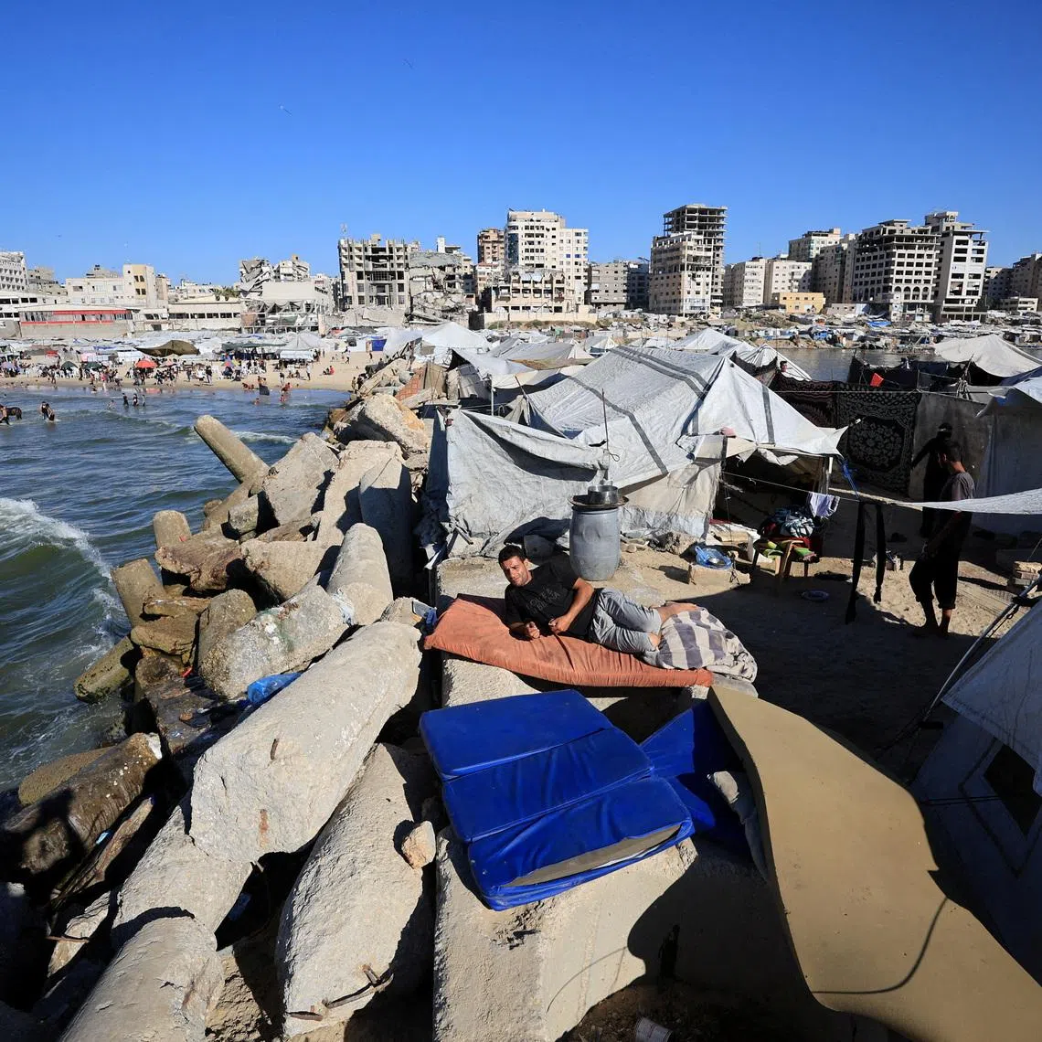 Shihab al-Suwaireki, a displaced Palestinian, rests on a mattress outside makeshift tents amid summer heat in Gaza City.