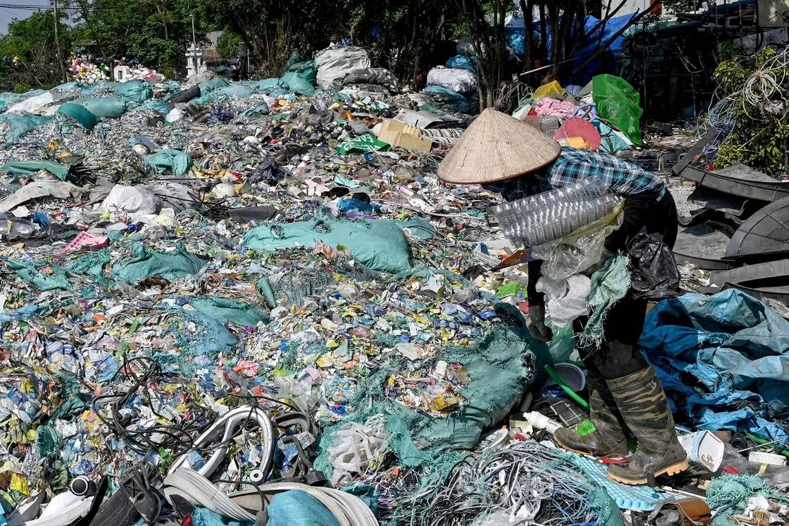 This photo taken on November 25, 2025, shows a woman picking up plastic waste at a landfill on the outskirts of Hanoi. Crouched between mountains of discarded plastic, Lanh strips the labels off bottles of Coke, Evian and local Vietnamese tea drinks so they can be melted into tiny pellets for reuse. (Photo by Nhac NGUYEN / AFP)