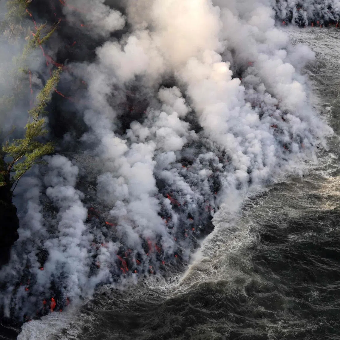 TOPSHOT - An aerial picture shows smoke rising as lava from the Piton de la Fournaise volcano reaches the ocean in Sainte-Rose, on the French Indian ocean island of Reunion, on March 16, 2026. The lava flow, which had stalled 150 metres from the ocean for several hours, finally reached the water on March 16, 2026 more than a month after the volcano began erupting on February 13, 2026. (Photo by Richard BOUHET / AFP)