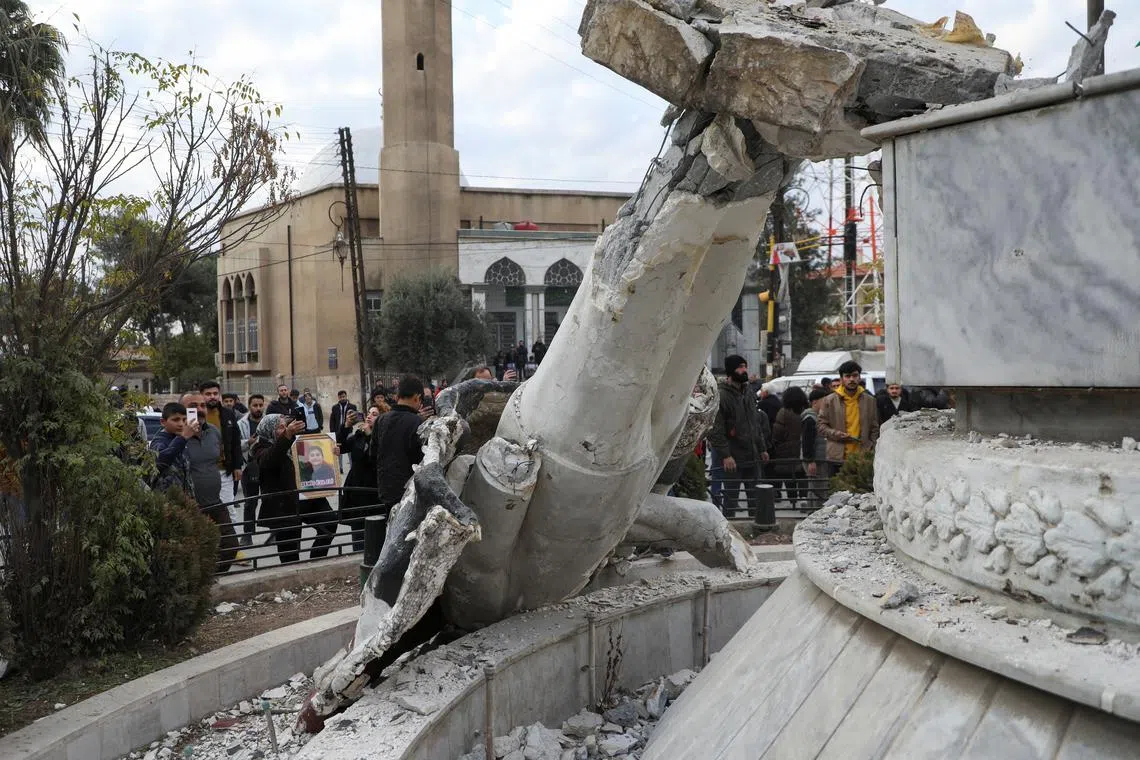 People stand near a damaged statue of former Syrian president Hafez al-Assad after Syrian rebels announced that they have ousted President Bashar al-Assad, in Qamishli, Syria on Dec 8, 2024.