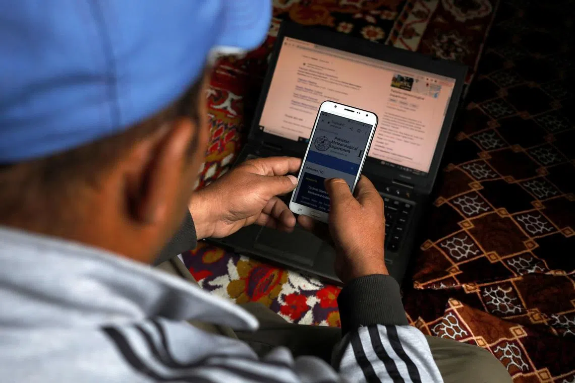 Tariq Jamil, 51, chairman of the Community Based Disaster Risk Management Centre, monitoring a metrological website on his mobile phone and laptop, at home in Hassanabad village, Hunza valley, in the Karakoram mountain range in the Gilgit-Baltistan region of Pakistan, Oct 9, 2023. His mission is to mobilise his community of 200 families in Hassanabad, in the Karakoram mountains, to fight for a future for their village and way of life, increasingly under threat from unstable lakes formed by melting glacier ice.     