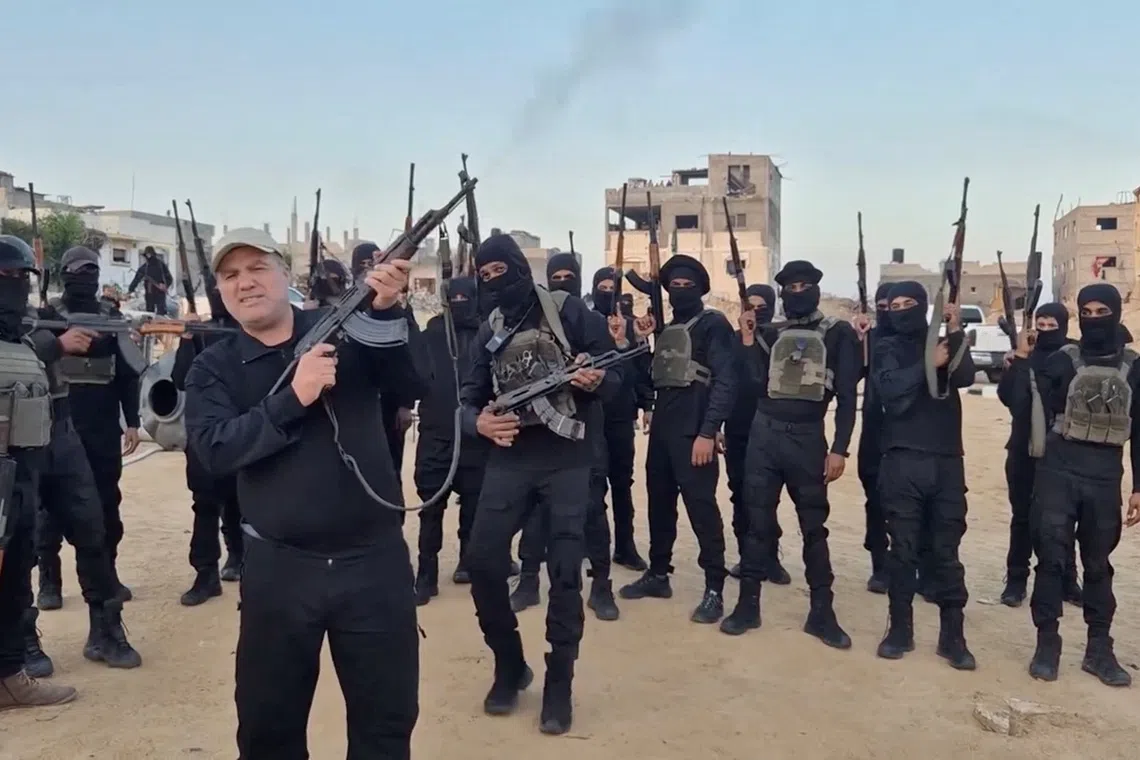 The head of an anti-Hamas faction, Hussam Alastal, fires a weapon in the air as he is surrounded by masked gunmen, in an Israeli-held area in Khan Younis, in the southern Gaza Strip, in this screenshot taken from a video released November 21, 2025. Hussam Alastal/via REUTERS