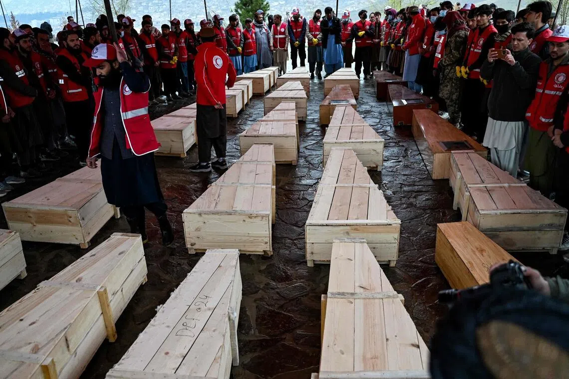 Afghan Red Crescent Society volunteers stand near the coffins of victims of a Pakistani air strike on a drug rehabilitation centre, during a mass burial at the Badam Bagh Hilltop in Kabul on March 18, 2026. 