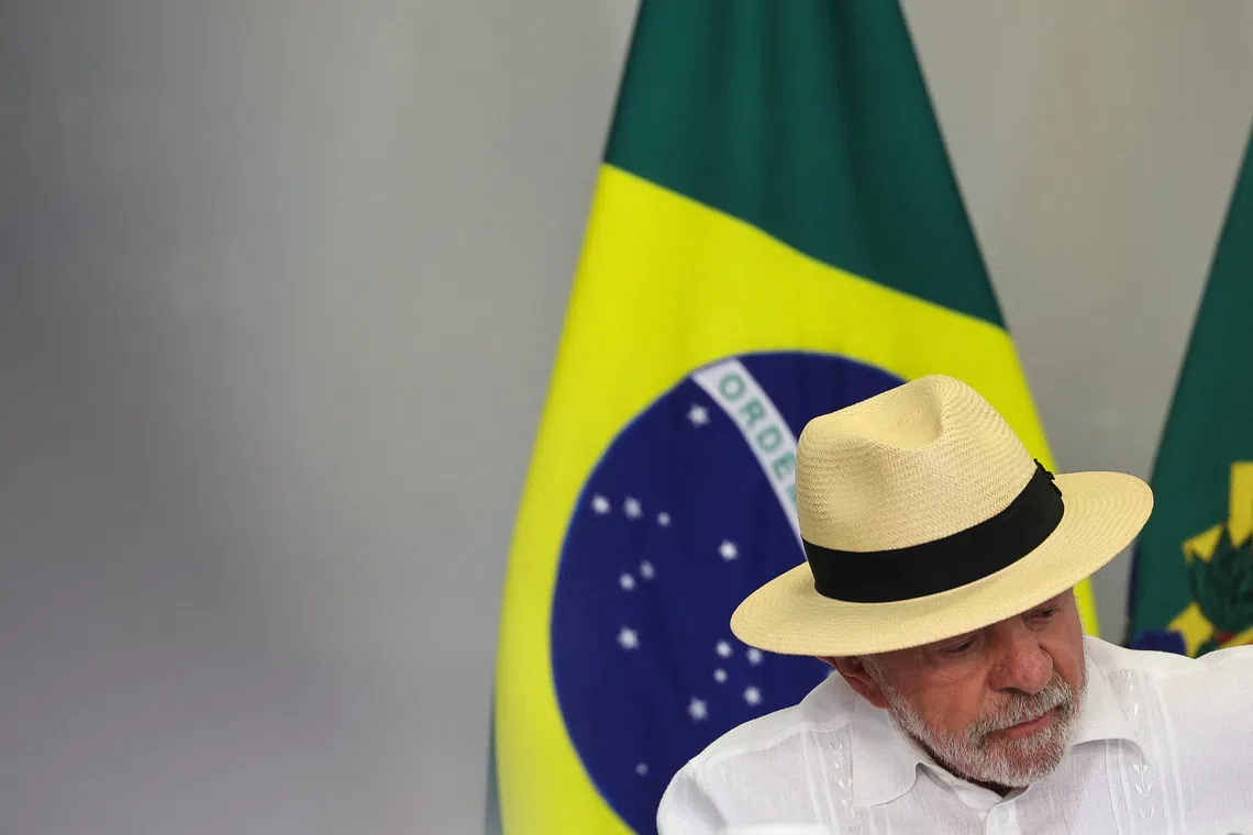 A man in a straw hat and white shirt stands in front of a Brazilian flag.