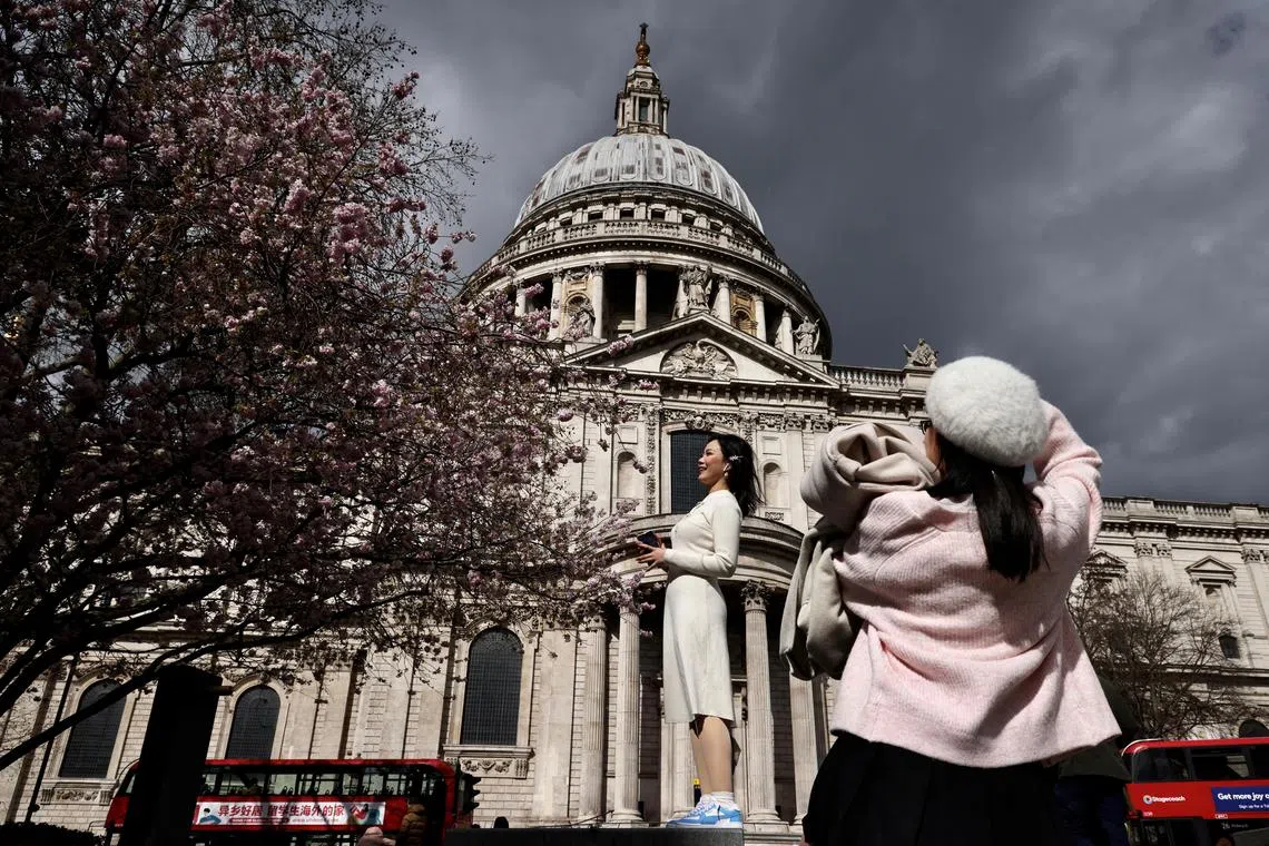 People who said they are Chinese students take pictures next to a Cherry Blossom tree outside St. Paul’s Cathedral in London, Britain, March 25 2023.  REUTERS/Kevin Coombs