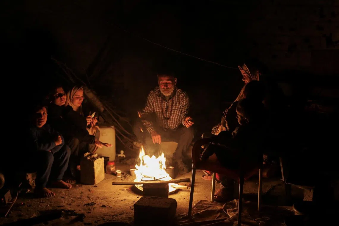 FILE PHOTO: Palestinians sit next to a fire, amid a ceasefire between Israel and Hamas, in Jabalia in the northern Gaza Strip, January 22, 2025. REUTERS/Mahmoud Issa/File Photo