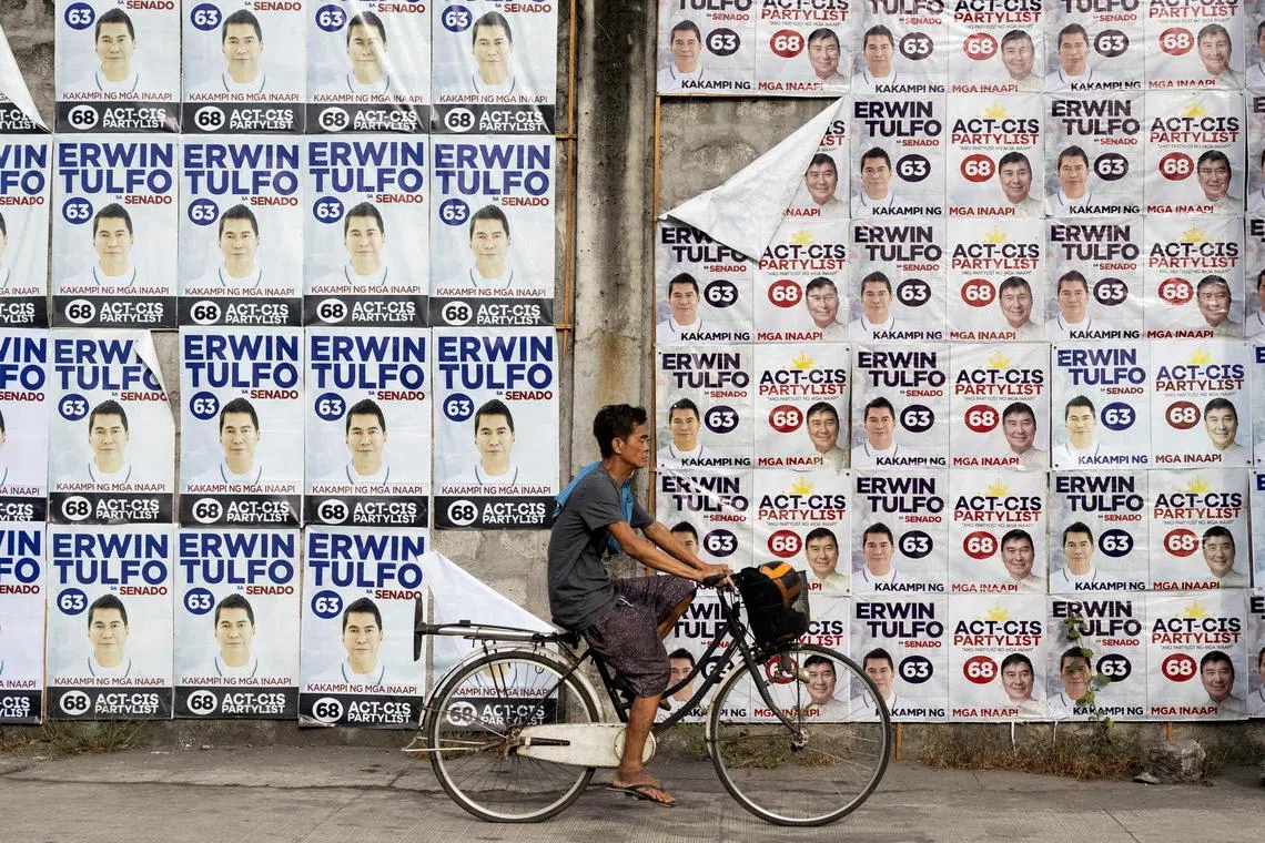 A man bikes past a wall of campaign posters for senatorial candidate Erwin Tulfo.