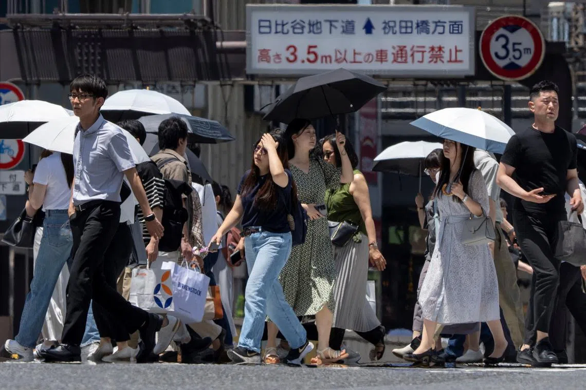 People walk along a street on a hot day in Tokyo on June 28.