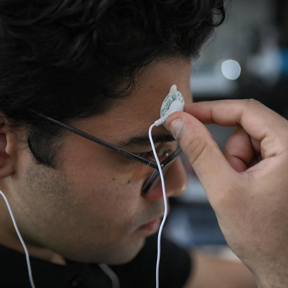 SUTD freshman Khambhati Mohammed Huzefa places electrodes on his forehead and behind his ears to demonstrate the device.