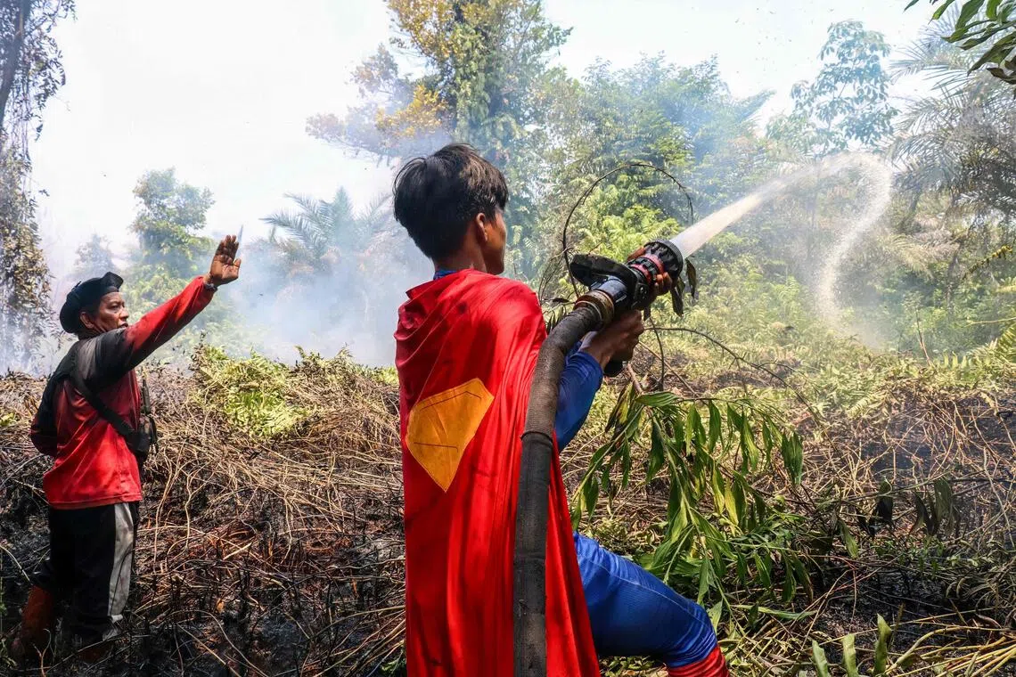 Indonesian student Rudiansyah (right) dressed in a Superman costume helps to extinguish a forest and land fire at Petuk Katimpun in Palangkaraya, Central Kalimantan, on Aug 17, 2026.