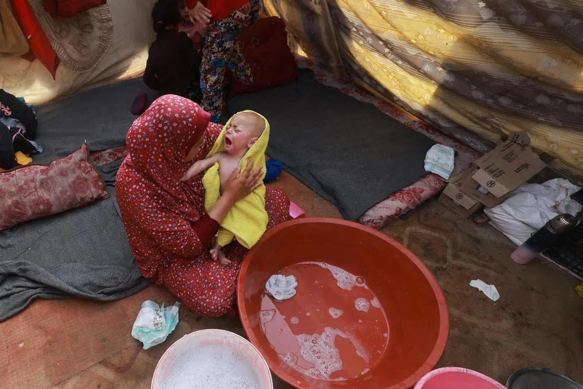 A woman dries a baby in a towel after giving it a bath, inside a tent at a camp for displaced Palestinians in Rafah in the southern Gaza Strip.
