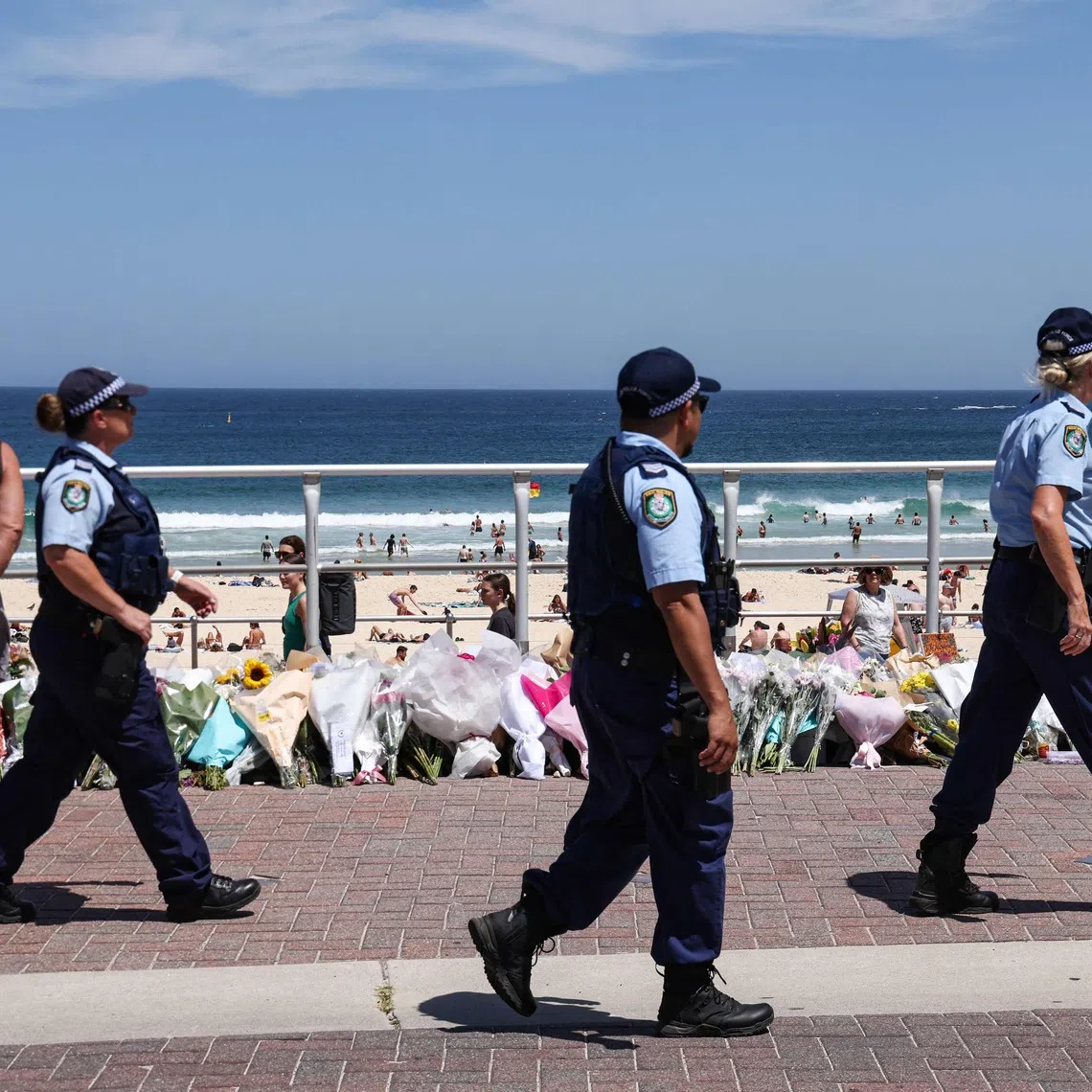Police officers walking past floral tributes left at the promenade of Bondi Beach in Sydney on Dec 18.