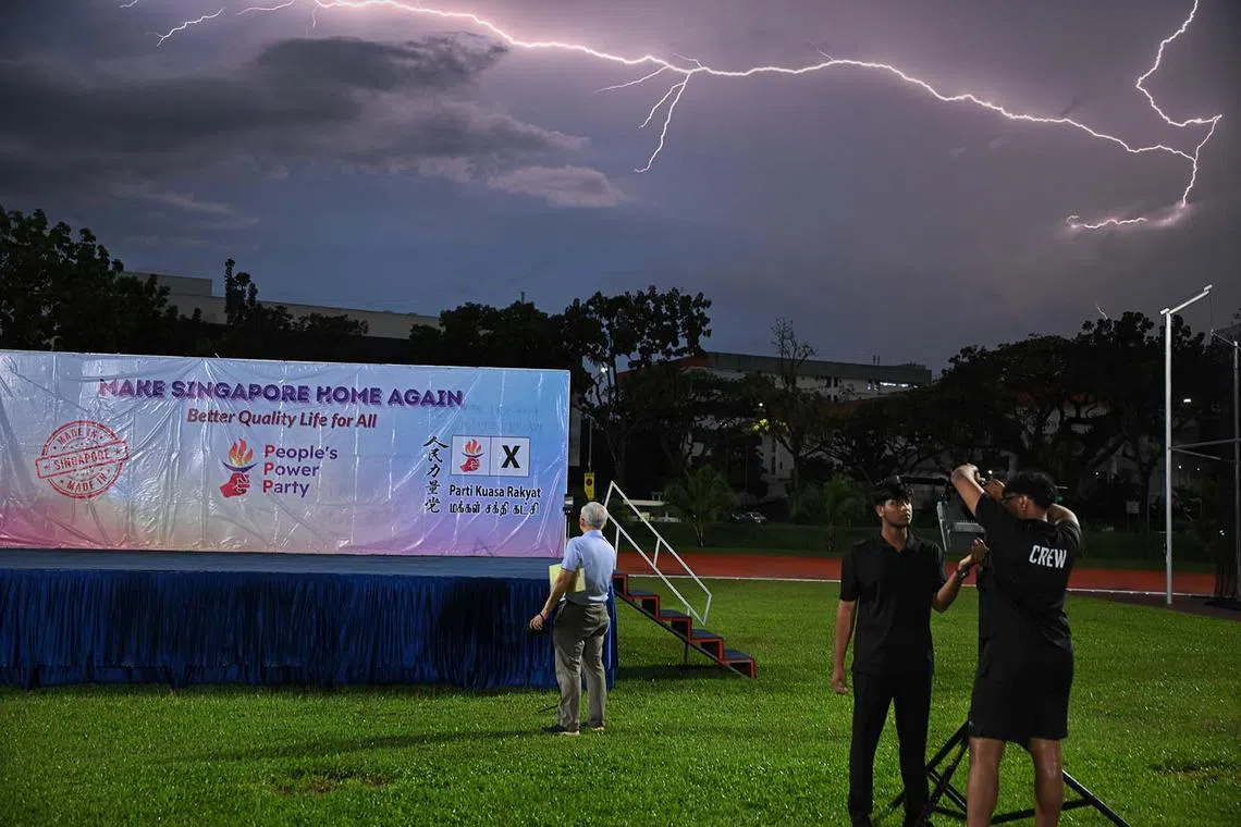 People’s Power Party (PPP)’s party secretary-general Goh Meng Seng (centre) setting up a phone camera at the side of the stage ahead of his party's rally at Yio Chu Kang Stadium as lightning strikes on April 29, 2025.