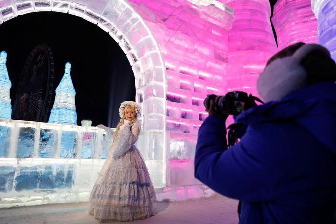 A woman dressed up in a costume poses for pictures in front of an ice sculpture depicting a castle, at the Harbin International Ice and Snow Festival, in Harbin, Heilongjiang province, China January 4, 2024. REUTERS/Tingshu Wang