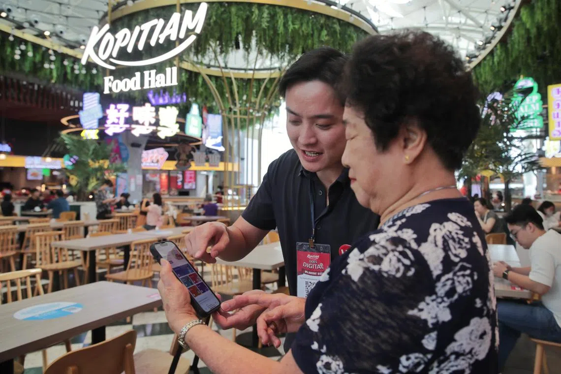 FairPrice digital buddy Keith Lee (left), 39  teaching Mdm Peh Ah Eng, 79, how to use the FairPrice app at the Kopitiam outlet in Jurong Point.