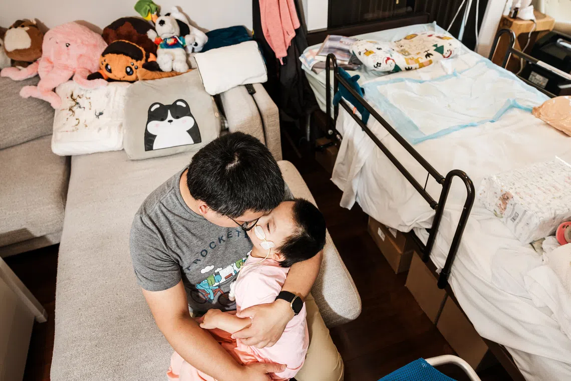 Hui Li holds his daughter Olivia, who at the age of 4 came down with the flu and developed acute necrotizing encephalopathy (ANE), in the familyÕs living room in Sunnyvale, Calif., Aug. 14, 2025. The rare neurological condition can develop from influenza and other viral infections, including COVID-19. (Carolyn Fong/The New York Times)
