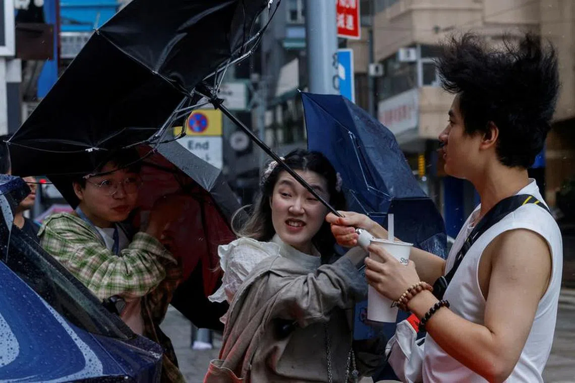 People struggle with umbrellas while walking against strong wind, as Typhoon Koinu approaches, in Hong Kong, China October 8, 2023. REUTERS/Tyrone Siu