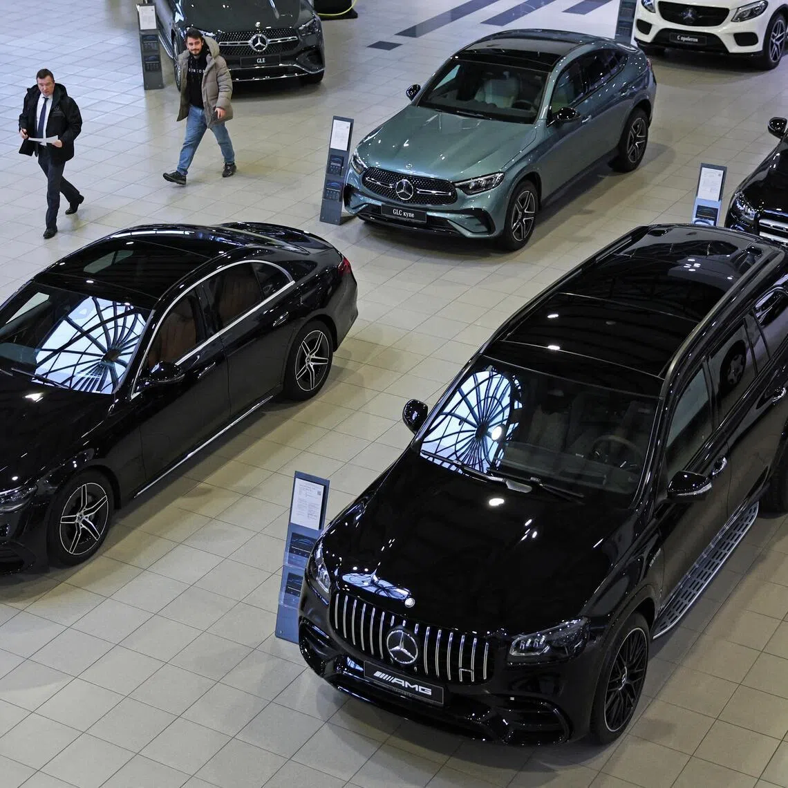An employee and a visitor walk past Mercedes-Benz cars at a Panavto dealership in Moscow, on Dec 19, 2025.