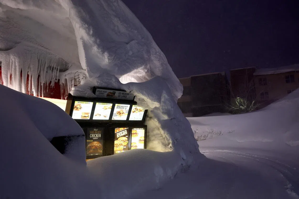 A Carl's Jr. drive-through menu is partially buried in a snowbank piled up from current and previous storms as snow continues to fall in the Sierra Nevada mountains, in the wake of an atmospheric river event, on March 11, 2023, in Mammoth Lakes, California. 