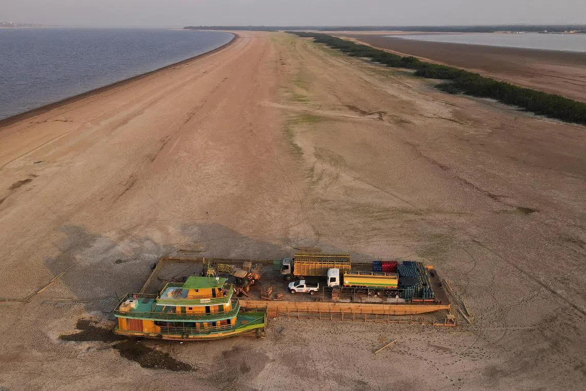 A tug boat and a barge carrying trucks and empty cooking gas cylinders and a backhoe, lie stranded on a sand bank of a diminished Rio Negro river.  
