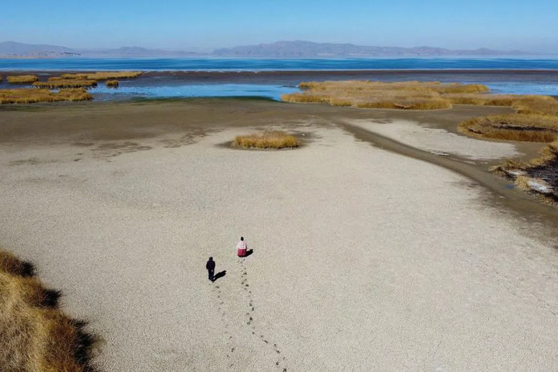 FILE PHOTO: Gabriel Flores and Isabel Apaza walk on the dry cracked bed near the shore of Lake Titicaca in drought season in Huarina, Bolivia August 3, 2023. REUTERS/Claudia Morales/File Photo