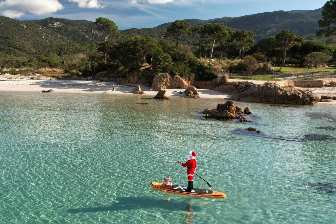This aerial photograph shows a woman dressed as Santa Claus steering a paddleboard close to the Mare e Sol beach in Pietrosella on December 20, 2022 on the French Mediterranean island of Corsica. 