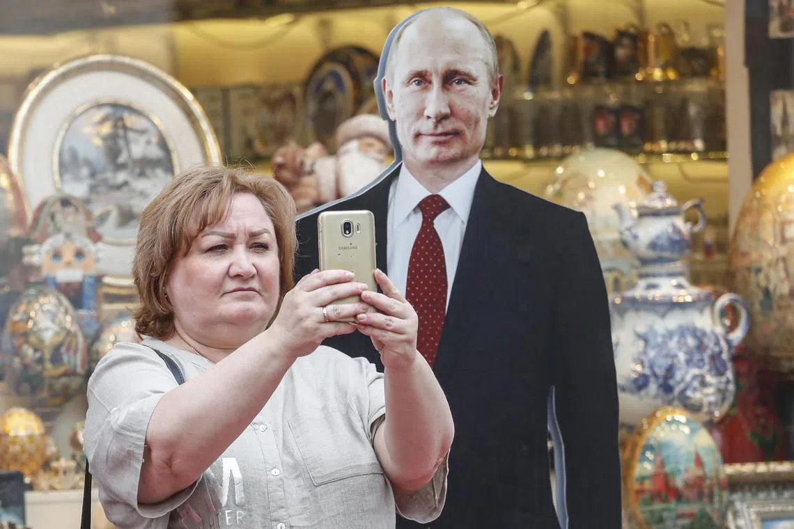 A woman takes pictures with a cardboard sculpture of Russian President Vladimir Putin in downtown of Moscow.