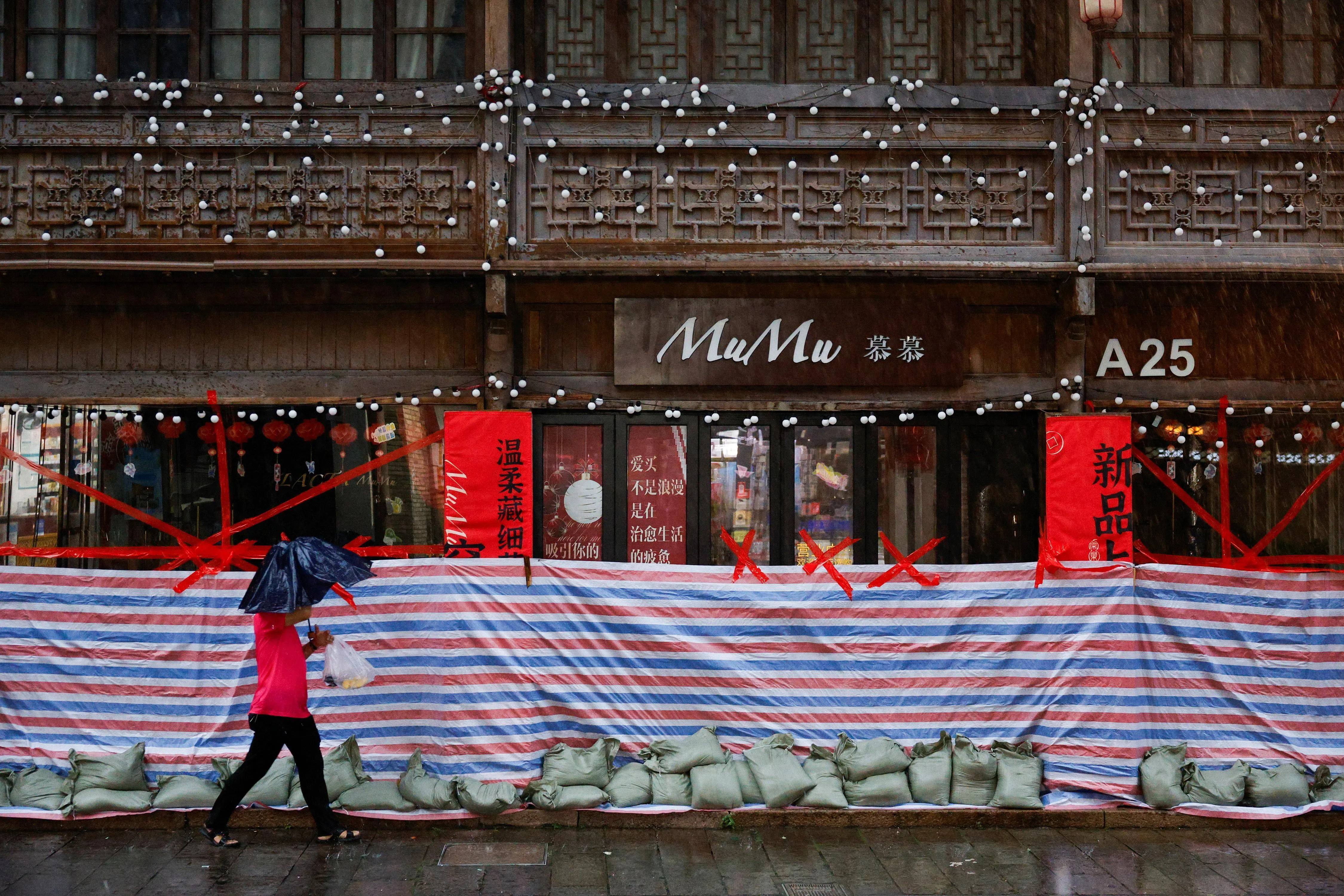 A person with an umbrella walks past a shop secured with sandbags, tape and plastic sheeting as rain intensifies ahead of the arrival of Typhoon Bavi in Wenzhou, Zhejiang province, China July 11, 2026. REUTERS/Go Nakamura