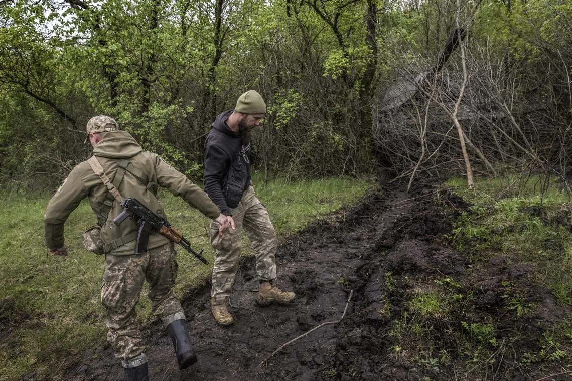 With their Panzerhaubitze, a German-made self-propelled howitzer, hidden under tree branches nearby, Ukrainian soldiers shake hands as they pass each another in the mud in a forest near the front line in UkraineÕs Zaporizhzhia region on Sunday, April 30, 2023. The unusually wet ground is one obstacle that the Ukrainian military, for all of its ingenuity, is finding difficult to overcome as it prepares for a counteroffensive against Russian forces. (David Guttenfelder/The New York Times)