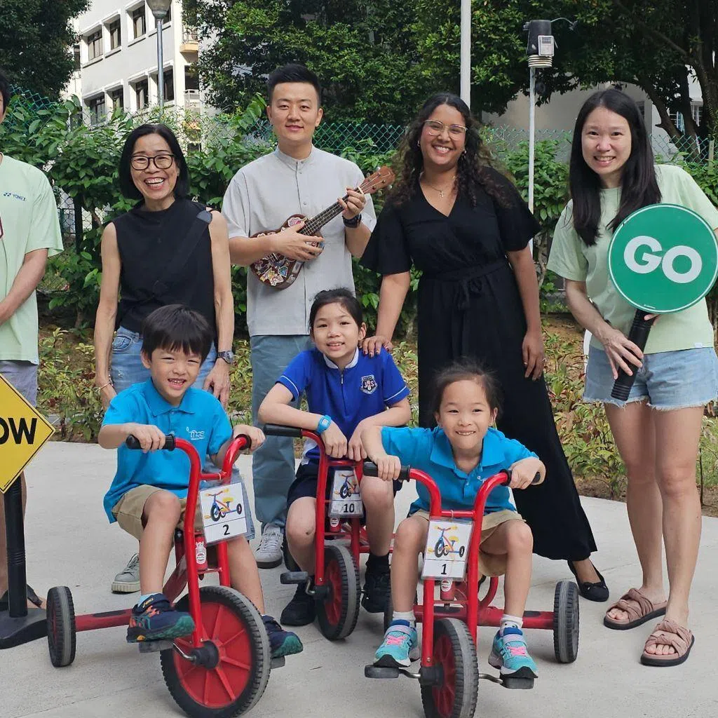 Mr Neo Sheng Xiong and Madam Chua Ming Boon (holding the “stop” and “go” signs respectively) credit the teachers at MK@Jing Shan and centre head Mak Kit Meng (second from left) for preparing their eldest daughter, Lyra (seated in the middle), for a smooth transition to primary school, leading them to enrol her younger twin siblings in the MK as well.