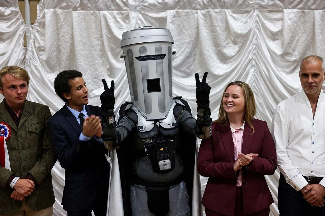 Count Binface gestures while standing with other candidates after Reform UK party leader Nigel Farage was declared the winner for the Clacton by-election, triggered by the resignation Farage, in Essex, Britain, August 14, 2026. REUTERS/Jack Taylor TPX IMAGES OF THE DAY