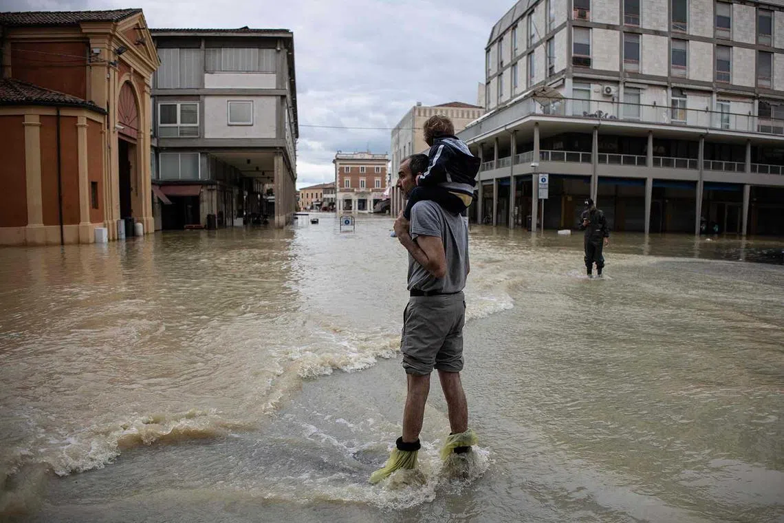 A resident carries a child in a flooded street in the town of Lugo on May 18, after heavy rains caused flooding across Italy's northern Emilia Romagna region. Rescue workers searched for people still trapped by floodwaters in northeast Italy as more residents were evacuated after downpours devastated homes and farms. 