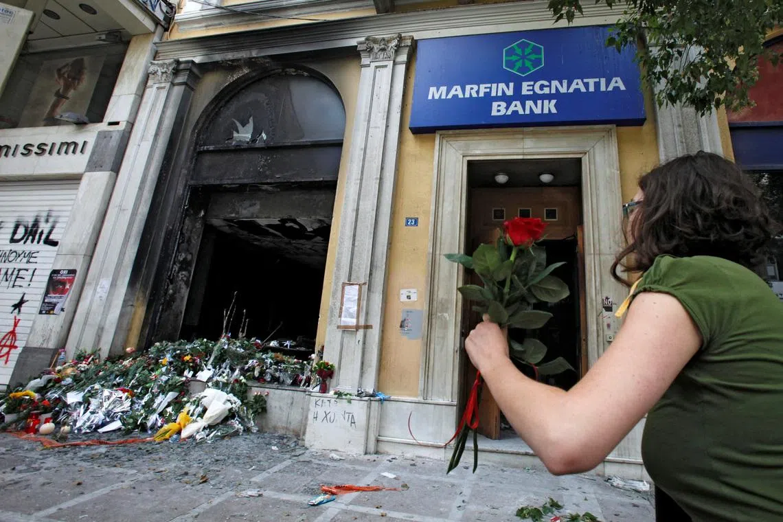 FILE PHOTO: A woman arrives to place a flower outside a burned-out bank, May 6, 2010 , which was set on fire during violent demonstrations in Athens a day earlier. REUTERS/Pascal Rossignol/File Photo