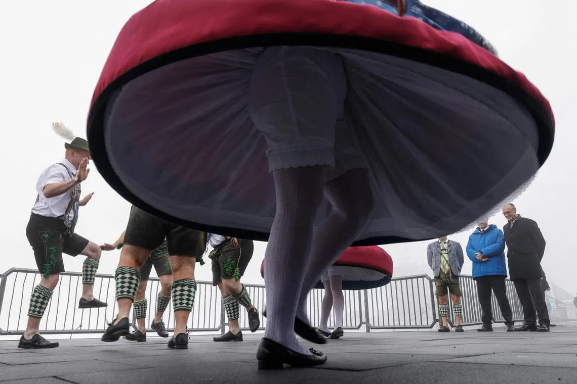 German Chancellor Friedrich Merz (right) and Bavaria's State Premier Markus Soeder (2nd from right- hidden) watching traditional Bavarian 'Schuhplattler' dancers performing atop the Zugspitze mountain in Grainau, southern Germany, on July 15, 2025.
