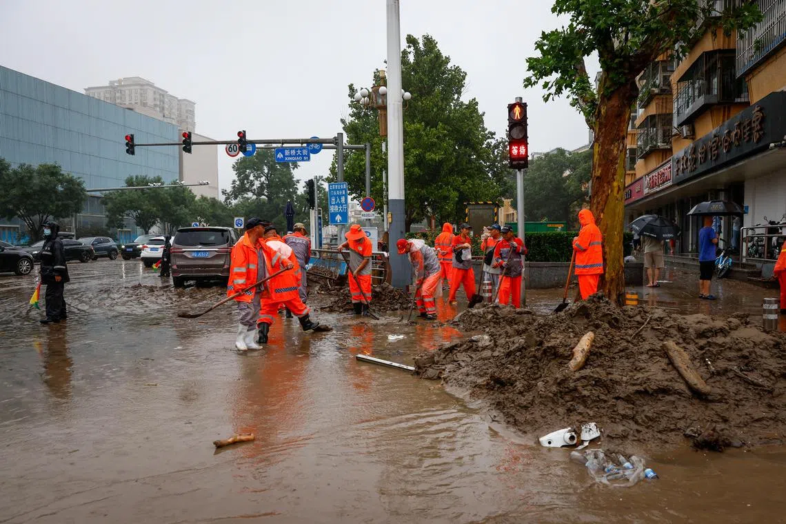 Workers clear mud from a road during a downpour in Mentougou, Beijing, on Aug 1.